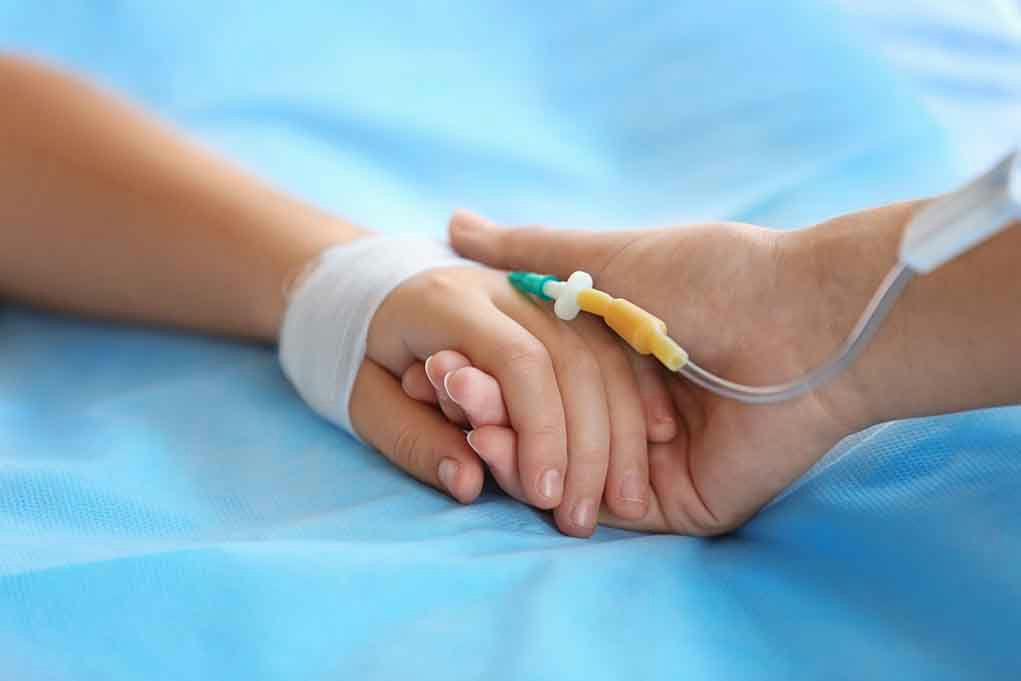 Two hands holding, one with medical IV attached.
